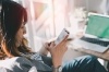 Woman using cellphone and sitting by open laptop