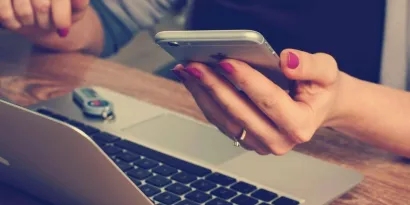 Close up of person holding their phone near their laptop