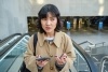 Woman at the top of the escalator holding her phone and looking confused