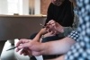 Three people sitting together while the middle person taps a mobile device.